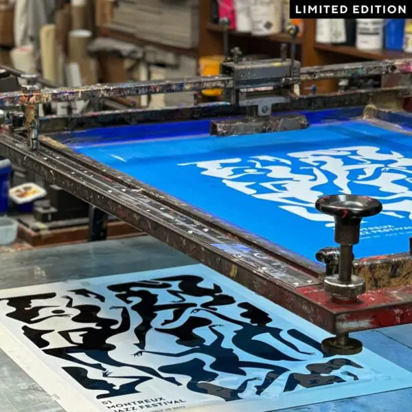Une presse à sérigraphie crée une affiche en édition limitée avec des formes noires abstraites et audacieuses sur un fond bleu clair. Des fournitures artistiques et des outils colorés sont visibles à l'arrière-plan.