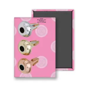 L'affiche Magnet John M Armleder, 2008, présente un fond rose avec trois serrures métalliques - argent, or et bronze - disposées verticalement. La mention "42e Festival de Jazz de Montreux du 4 au 19 juillet 2008" est imprimée au-dessus. Présentée à côté d'un cadre à fond noir.