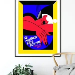 Affiche encadrée du Montreux Jazz Festival 2023 avec figure abstraite rouge, fond bleu et noir, bordure jaune, et texte indiquant 55 Montreux Jazz Festival 1-16 juillet 2023, affichée au-dessus d'une plante et d'une chaise.