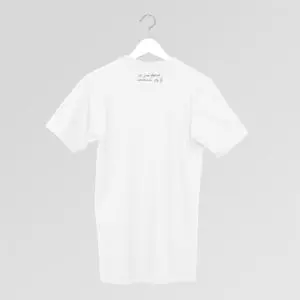 Un T-shirt blanc uni sur un cintre, présenté sur un fond gris clair. Un petit texte manuscrit se trouve près de l'encolure, au dos du tee-shirt.
