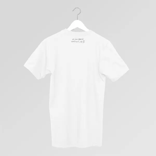 Un T-shirt blanc uni sur un cintre, présenté sur un fond gris clair. Un petit texte manuscrit se trouve près de l'encolure, au dos du tee-shirt.