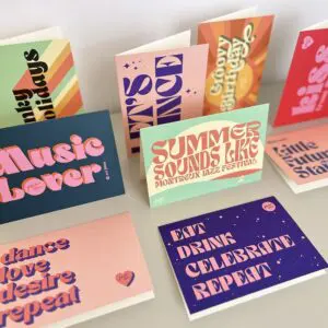 Une présentation de cartes de vœux colorées avec des polices de caractères audacieuses de style rétro comportant des phrases telles que "Music Lover", "Summer Sounds Like Montreux Jazz Festival" et "Eat Drink Celebrate Repeat" sur une surface blanche.