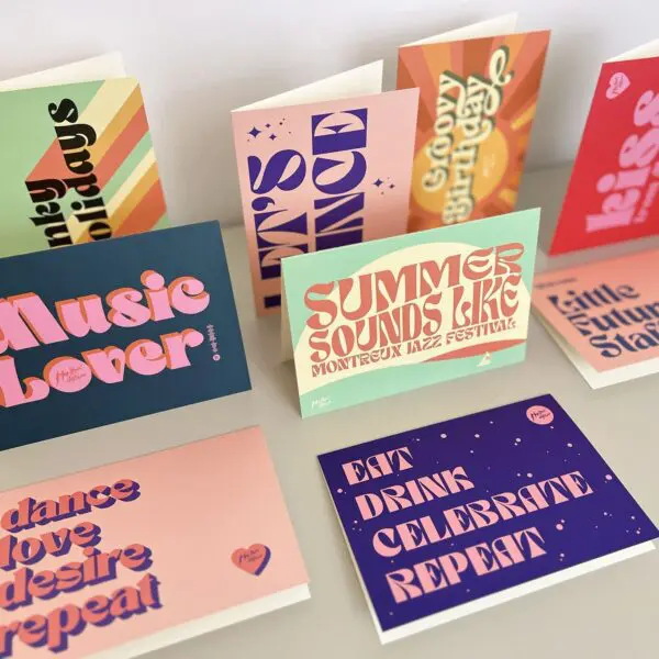 Une présentation de cartes de vœux colorées avec des polices de caractères audacieuses de style rétro comportant des phrases telles que "Music Lover", "Summer Sounds Like Montreux Jazz Festival" et "Eat Drink Celebrate Repeat" sur une surface blanche.