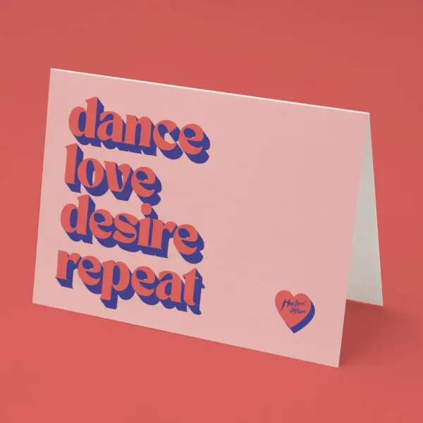 The Dance Love Desire Repeat Card features bold, shadowed text in purple and red on a folded card set against a pink surface, with a small red heart in the corner displaying "Monkira Studio.