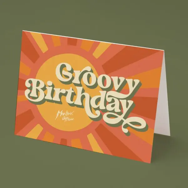 Cette carte d'anniversaire colorée au design rétro comporte les mots "Groovy Birthday" en grandes lettres ludiques sur un fond de soleil orange et jaune. La carte est posée sur une surface verte.