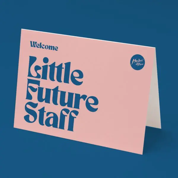 The Little Future Staff Card features bold blue text on a pink background reading “Welcome Little Future Staff Music,” with a small blue circle of white script in the top right, displayed standing on a blue surface.