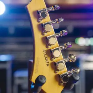 Close-up of the back of a Limited Series Atlanta Guitar Collection headstock with tuning pegs and "ATLANTA" engraved, set against blurred stage lights—evoking Montreux Jazz Guitar style in an Atlanta-inspired design.