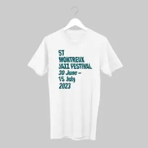 Un T-shirt blanc sur un cintre affiche le texte 57 Montreux Jazz Festival 30 juin - 15 juillet 2023 en caractères gras sarcelle sur un fond gris uni.
