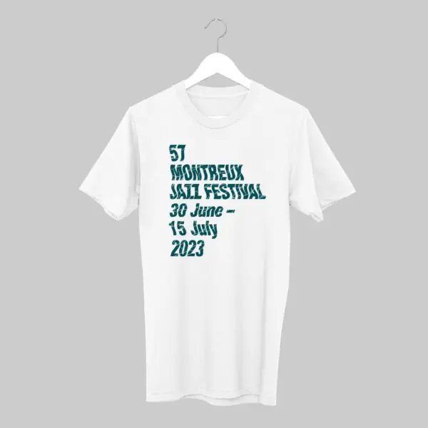 Un T-shirt blanc sur un cintre affiche le texte 57 Montreux Jazz Festival 30 juin - 15 juillet 2023 en caractères gras sarcelle sur un fond gris uni.