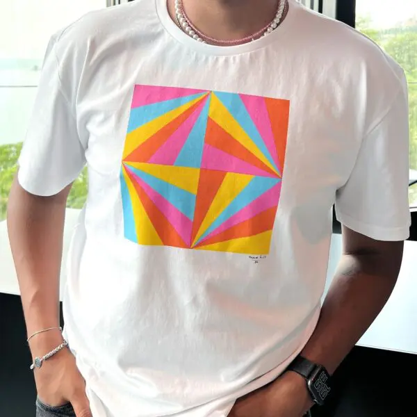 Une personne portant un tee-shirt blanc avec un motif géométrique coloré composé de triangles roses, jaunes, bleus et orange. Elle porte également une montre, des bracelets et un collier de perles.