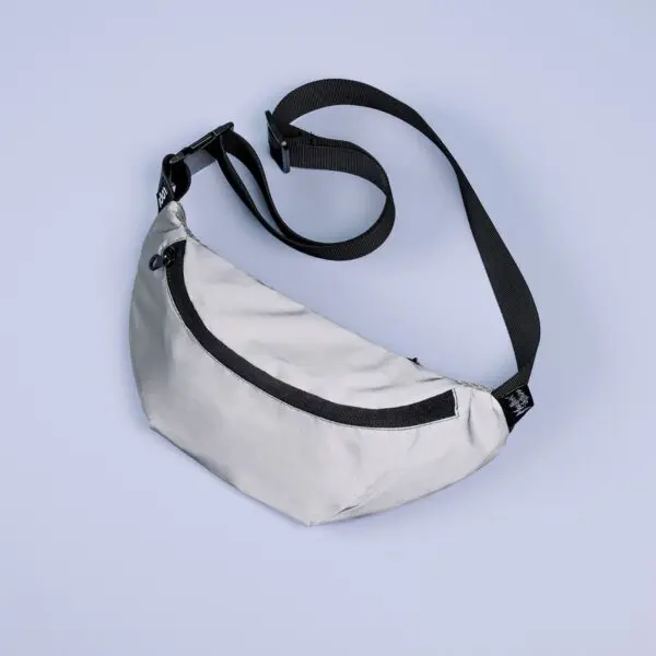 A Reflective Mini Bumbag in light gray with a black zipper and adjustable strap is shown on a pale blue background.