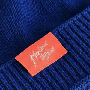 Gros plan d'un tricot bleu sur lequel est cousue une étiquette rectangulaire rouge. L'étiquette comporte un texte écrit à la main en blanc, avec la mention Montreux Jazz Festival.