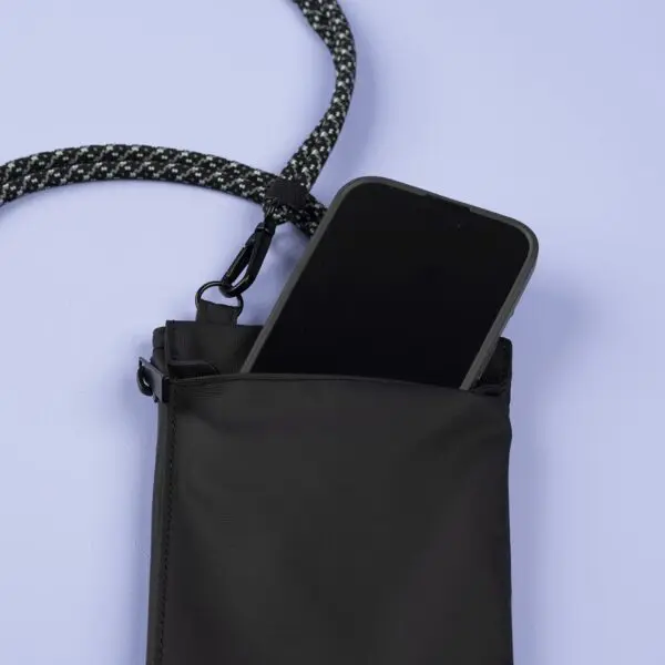 A black smartphone partially inside a Festival Bag, Lakeside edition, featuring a patterned black-and-white rope strap, set against a light purple background.