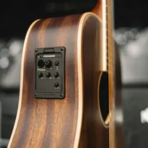 Gros plan sur le côté d'une guitare acoustique, montrant un système de préamplification Fishman Presys avec des boutons de contrôle pour le volume, les basses, le médium et les aigus, placé dans un corps avec une finition en bois naturel.