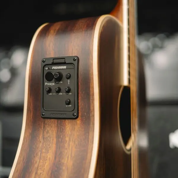 Gros plan sur le côté d'une guitare acoustique, montrant un système de préamplification Fishman Presys avec des boutons de contrôle pour le volume, les basses, le médium et les aigus, placé dans un corps avec une finition en bois naturel.
