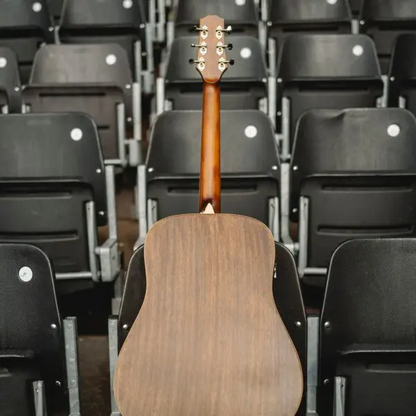 Une guitare acoustique marron, vue de l'arrière, repose debout contre des rangées de sièges de stade noirs et vides.