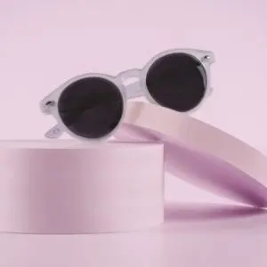 Des Lunettes Fly Bruxelles Cristal - Polarisant rondes et blanches reposent sur deux plates-formes cylindriques rose pâle sur un fond rose tendre, créant une présentation moderne et élégante inspirée du design contemporain chic.
