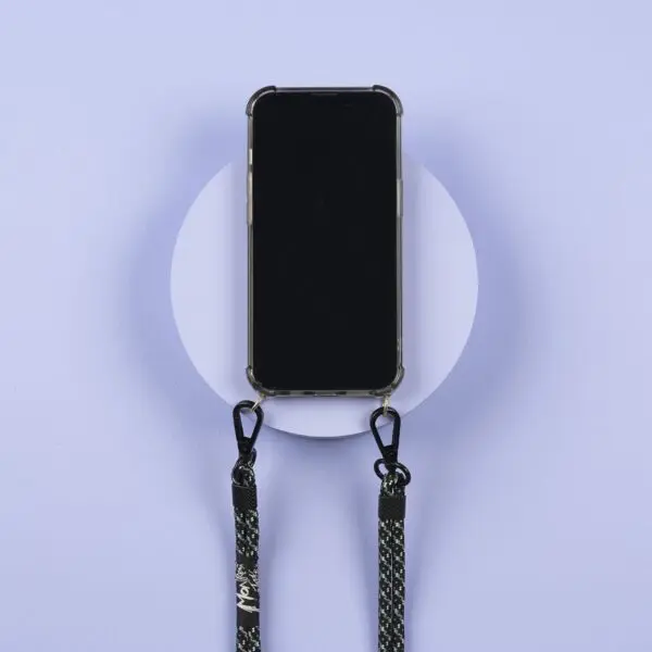 A smartphone in a clear case hangs on a light purple wall, attached to two black-and-white “Lakeside” Mobile Straps with metal clasps—perfect for showing off your style at Festival Montreux.