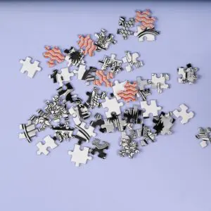 Une pile éparpillée de pièces de puzzle partiellement illustrées avec des motifs noirs, blancs et rouges sur une surface violette claire.
