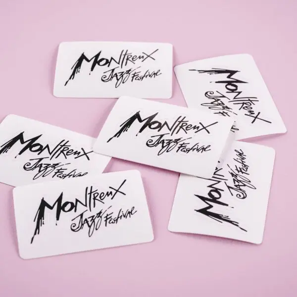 Six White Sticker Montreux Jazz Festival cards, featuring Rylsee’s stylized black lettering, are scattered on a pink surface.