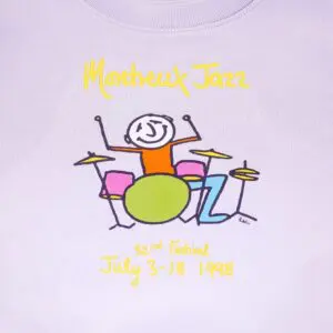 White graphic sweatshirt for kids features “Montreux Jazz” in yellow above a stick figure playing colorful drums. Below, “32nd Festival July 3-18 1998” appears in yellow—Phil Collins performed that year.