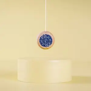 Un yo-yo en bois avec un motif circulaire bleu est suspendu par sa ficelle au-dessus d'un socle cylindrique jaune clair, sur un fond jaune pâle.