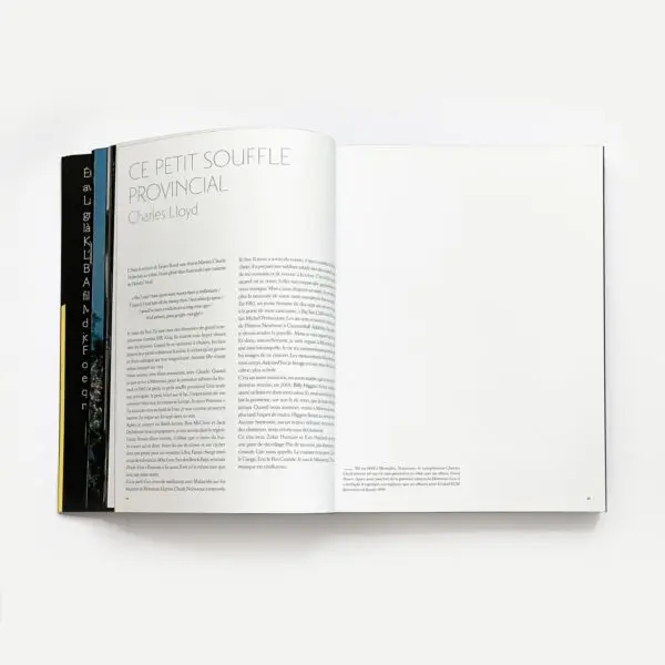 Un livre ouvert repose à plat, montrant une page intitulée CE PETIT SOUFFLE PROVINCIAL par Charles Lloyd avec du texte à gauche et une page de droite presque vierge ; trois dos noirs d'autres livres sont partiellement visibles à gauche.