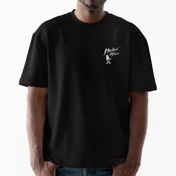 Une personne se tient debout sur un fond blanc uni et porte le t-shirt Lineup 2024 en édition limitée, avec une coupe ample noire, un petit graphique blanc et le texte "Monlixx Costume" sur la poitrine gauche, de la collection Festival Montreux.