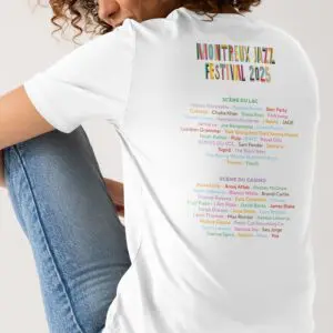 Une personne portant un T-Shirt blanc Lineup 2025, Édition limitée est assise dos à la caméra. Le tee-shirt montre la programmation du Montreux Jazz Festival 2025, le nom de chaque artiste étant affiché dans une couleur unique et vibrante.