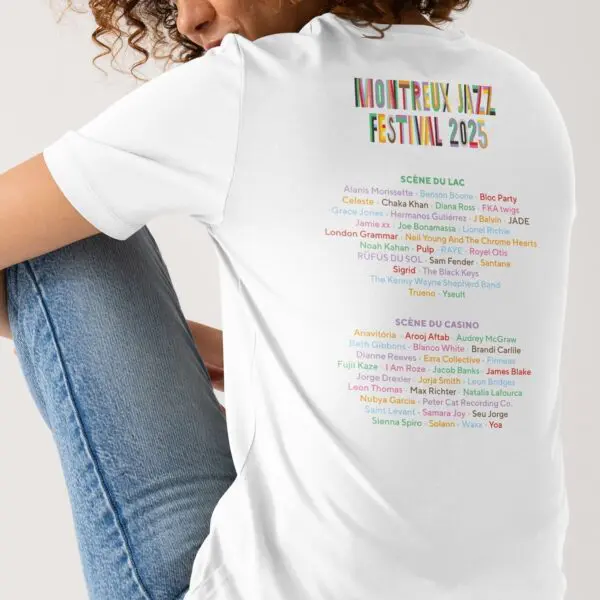 Une personne portant un T-Shirt blanc Lineup 2025, Édition limitée est assise dos à la caméra. Le tee-shirt montre la programmation du Montreux Jazz Festival 2025, le nom de chaque artiste étant affiché dans une couleur unique et vibrante.