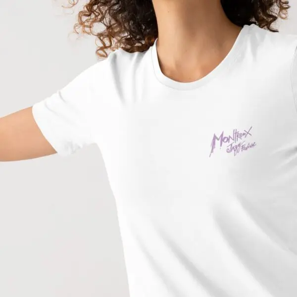 Une personne aux cheveux bouclés porte le T-shirt Lineup 2025, édition limitée, avec le logo violet du Montreux Jazz Festival sur la poitrine, sur un fond clair et uni.