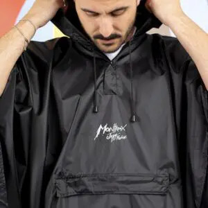 Une personne remonte la capuche d'un Poncho de pluie noir brillant réutilisable avec une poche frontale et le logo du Montreux Jazz Festival imprimé en blanc.