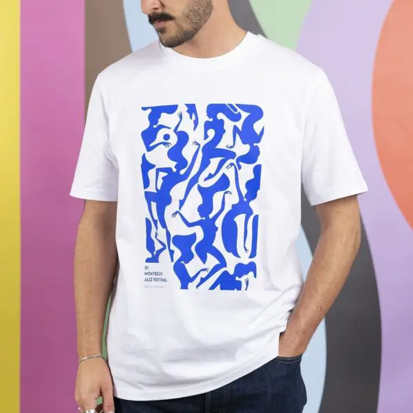 Une personne portant un T-Shirt Malika Favre, Bleu, 2017 présentant des motifs bleus abstraits et le texte du 57e Festival de jazz de Montréal se tient devant un mur coloré aux motifs ondulés.