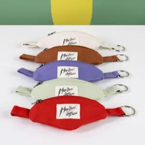 Cinq Porte-clés Mini Sac Banane colorés avec fermetures éclair et porte-clés sont alignés. Chaque pochette est étiquetée Montriex Est. France et disponibles en beige, marron, violet, vert et rouge - parfait pour les fans du Montreux Jazz.
