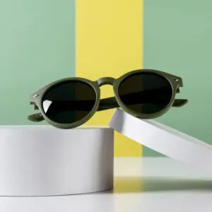 Les lunettes de soleil Lunettes Fly Bruxelles Kaki aux verres sombres sont posées sur des plates-formes cylindriques blanches devant des murs rayés vert et jaune, dans une ambiance Montreux Jazz.