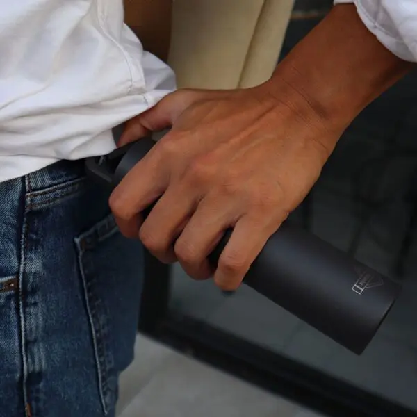 Vêtue d'un jean bleu et d'une chemise blanche, une personne met dans sa poche, de la main droite, une Mini Bouteille Isotherme noire mate de 180 ml, isolée.